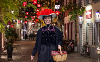 Eine Frau mit „Bollenhut“, im Hintergrund die weihnachtlich geschmückte Freiburger Altstadt